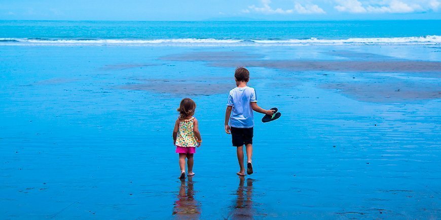 Dreng og pige går i vandet på stranden i Costa Rica